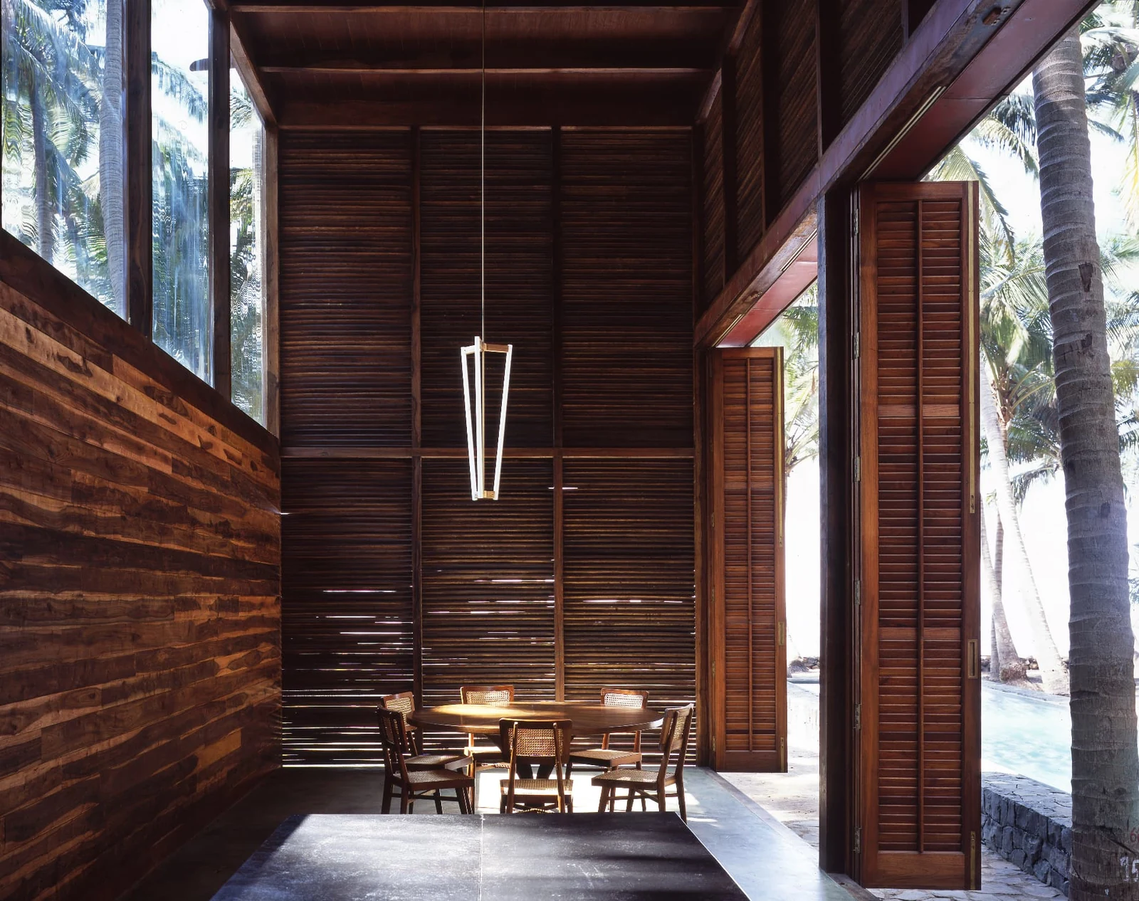 Tropical timber house interior with a slender pendant light above a round dining table