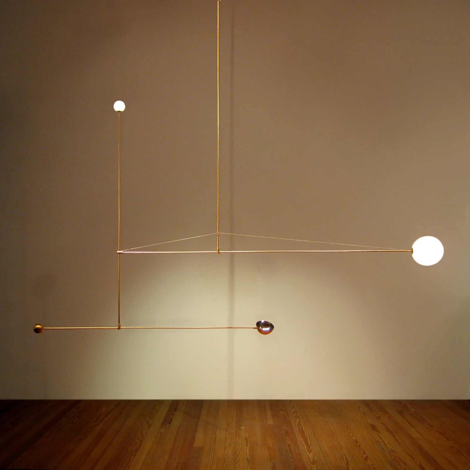 Ball Light — a balanced brass mobile with opal glass spheres suspended against a plain wall