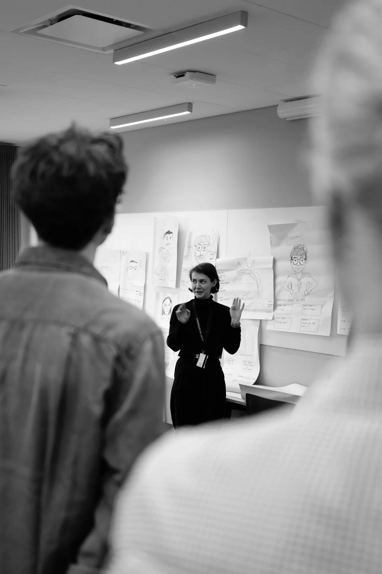 A designer presenting to colleagues in front of a wall of hand-drawn persona sheets