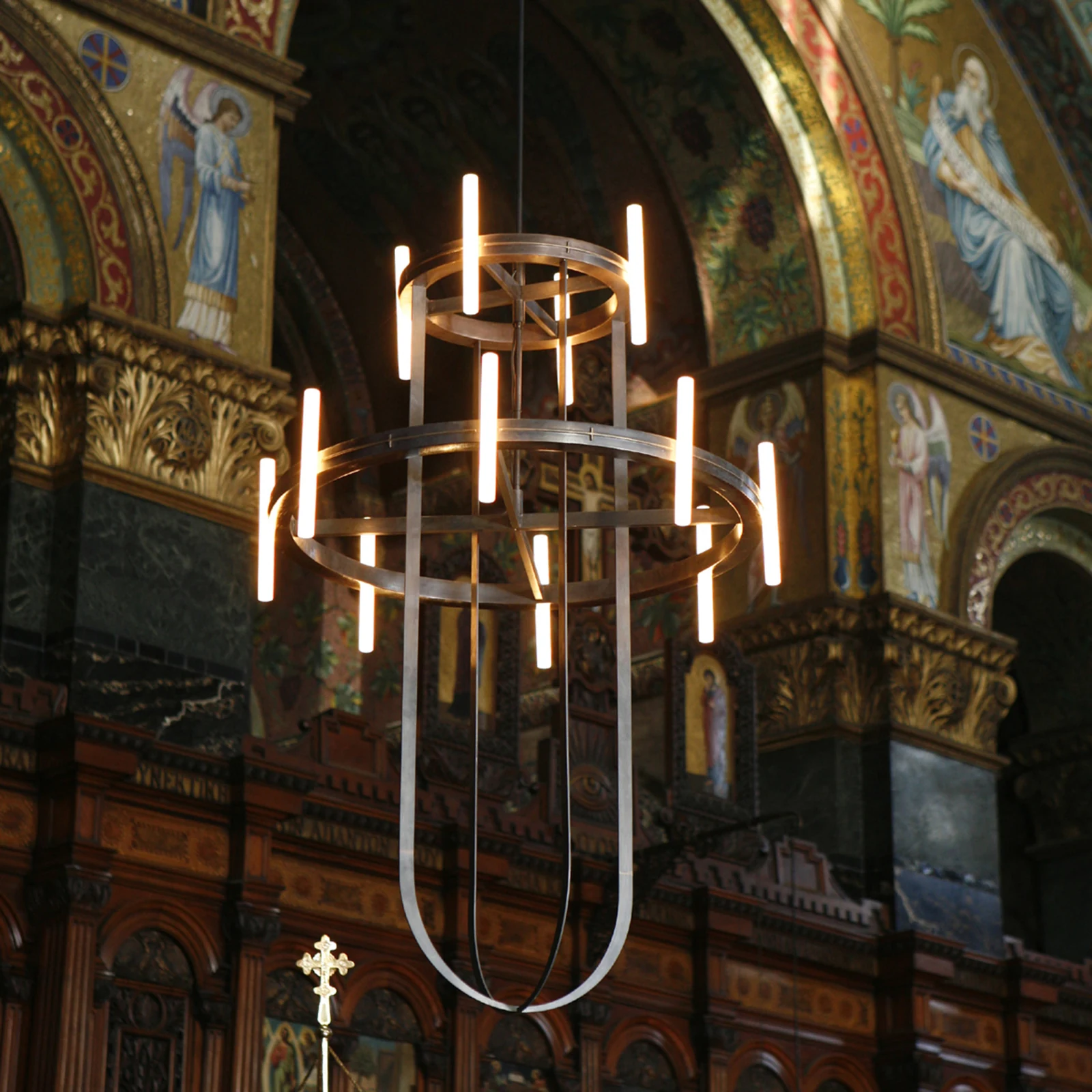 Two-tier metal chandelier with slim light tubes hanging in a mosaic-lined church interior