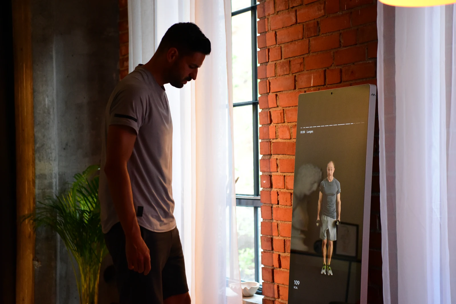 A person standing beside a connected fitness mirror mid-session