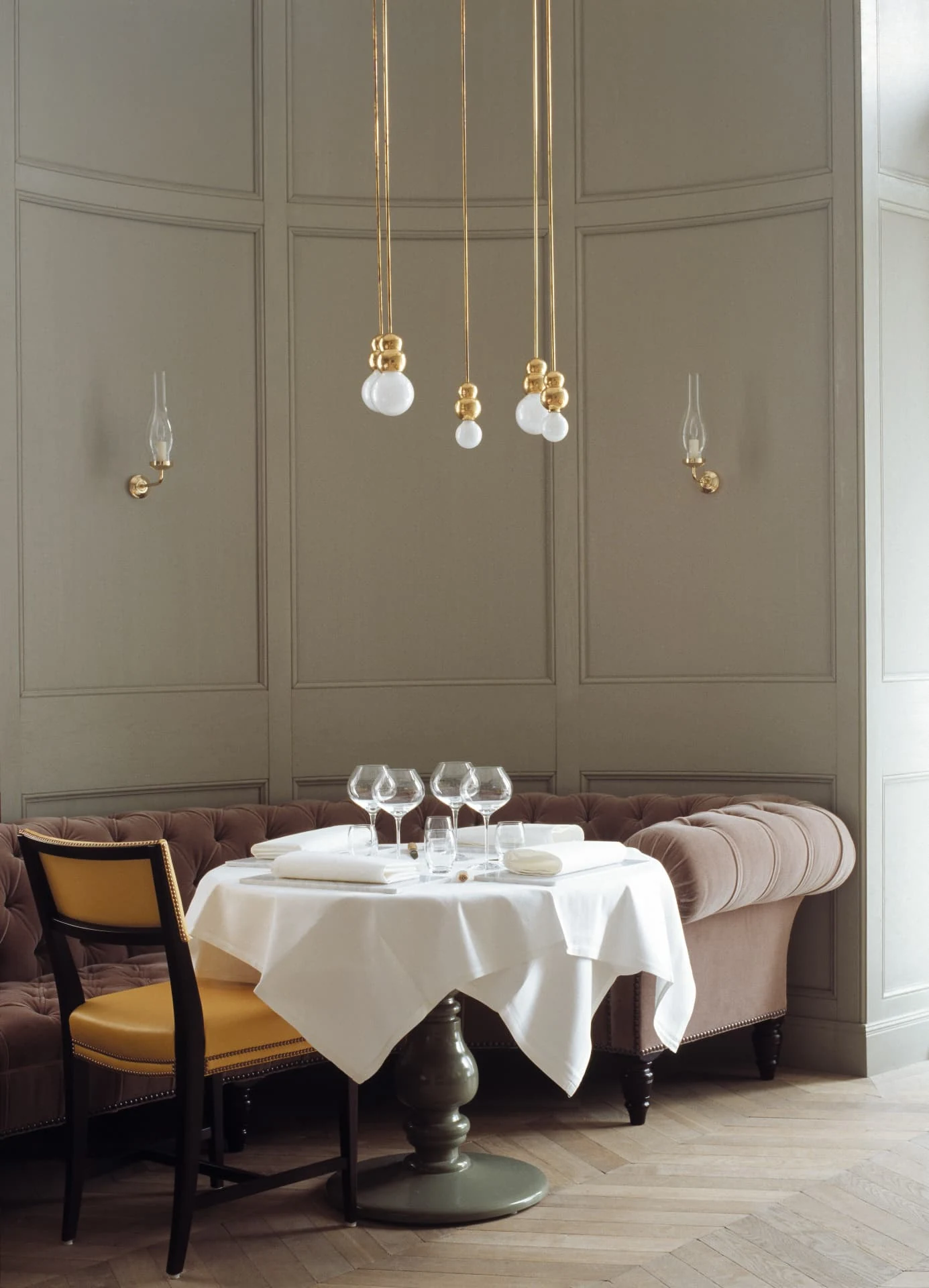 Restaurant dining room with a cluster of brass and opal glass pendant lights above a laid table